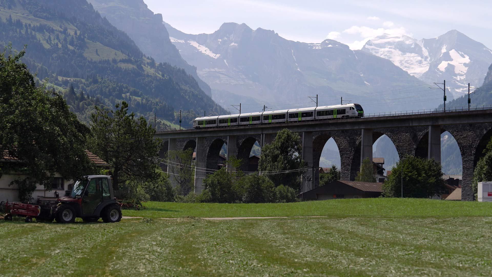 BLS-Zug fährt über Brücke vor Alpen-Berglandschaft.