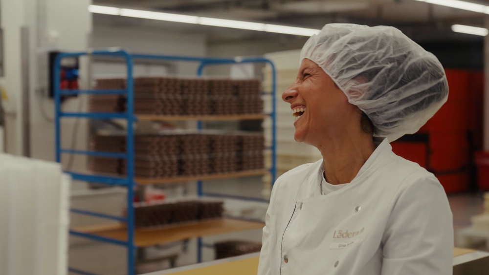 Mitarbeiterin in der Läderach-Schokoladenproduktion lacht, mit Haarnetz und Arbeitskittel.
