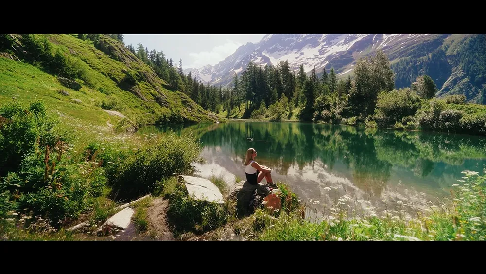 Person sitzt am Ufer eines Bergsees in alpiner Umgebung – Szene aus dem Imagefilm von BLS