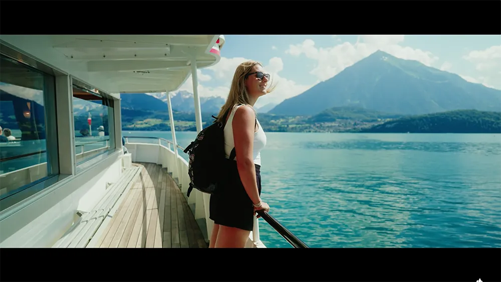 Frau steht an der Reling eines Schiffes und blickt über einen See mit Bergkulisse