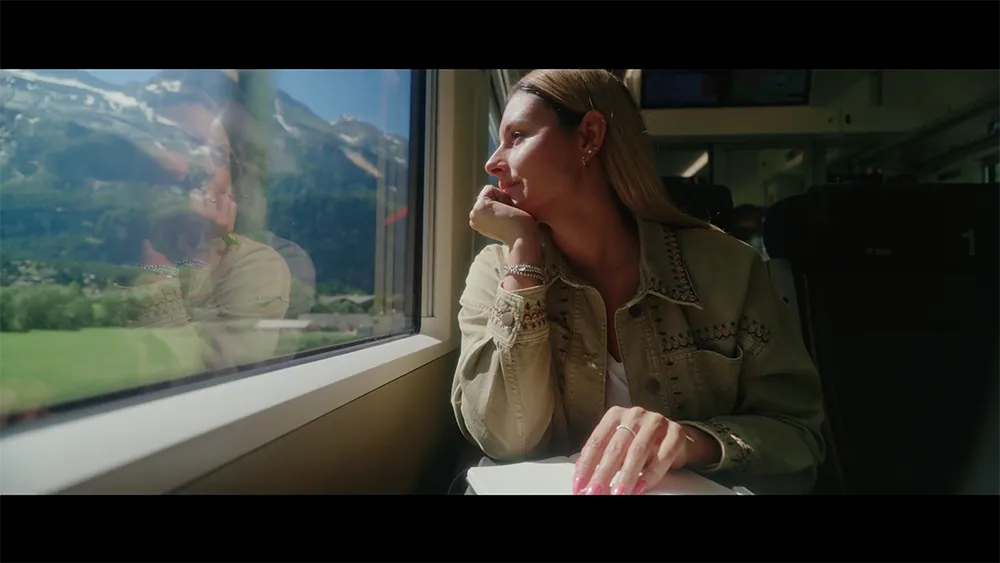 Frau sitzt im Zug der BLS und blickt aus dem Fenster auf die vorbeiziehende Landschaft