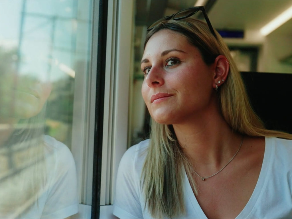 Frau sitzt im Zug und blickt aus dem Fenster – ruhige Szene aus dem Imagefilm von BLS