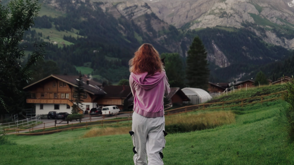 Person blickt von einer Wiese auf ein alpines Dorf – Szene aus dem Recruitingprojekt Projekt Alp