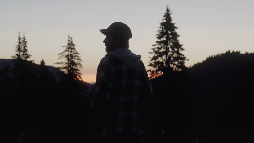 Silhouette einer Person bei Dämmerung vor Bäumen und Bergen – Recruiting-Visual aus Projekt Alp